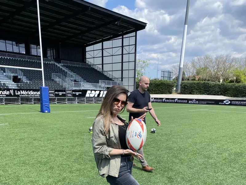 Sur la pelouse d’un stade, une personne pose avec un ballon de rugby