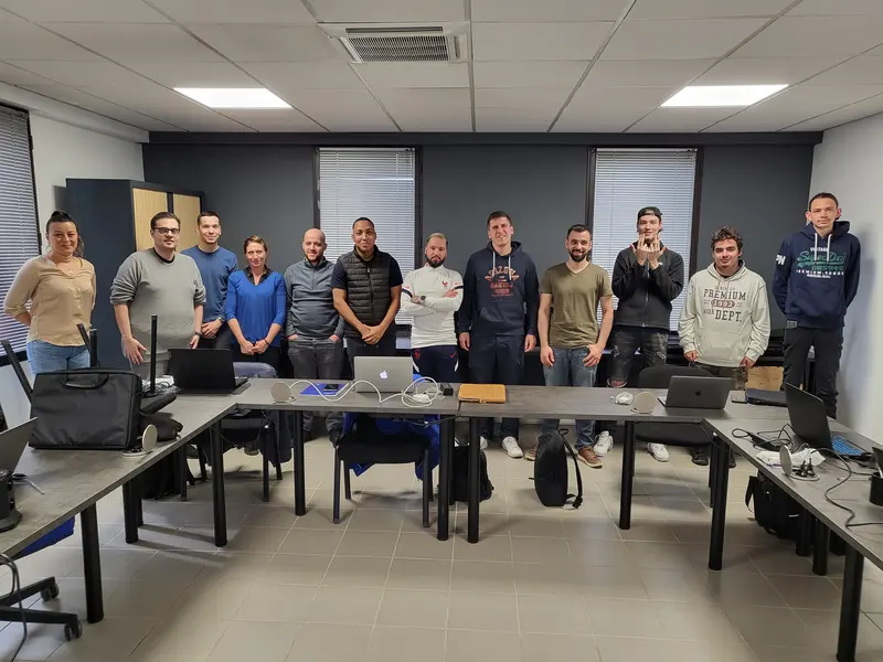 Une promotion au complet, debout derrière les tables de la salle de formation